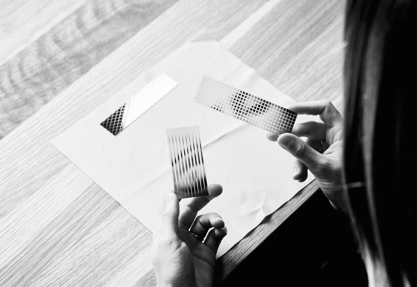Hands holding perforated metal samples over a sheet of paper